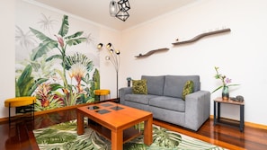 A living room with a grey sofa, a wooden coffee table, a yellow chair, a plant wall, and a modern light fixture.