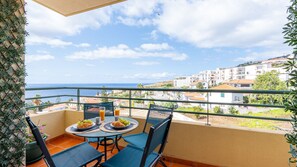 A balcony with a table set for two, overlooking a coastal town and the sea. - Delmar by LovelyStay (Caniço)