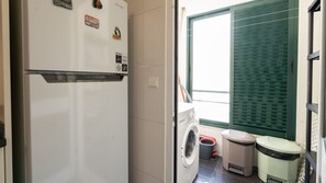 Une cuisine de taille réduite équipée d’un réfrigérateur, d’un lave-linge et d’une poubelle.