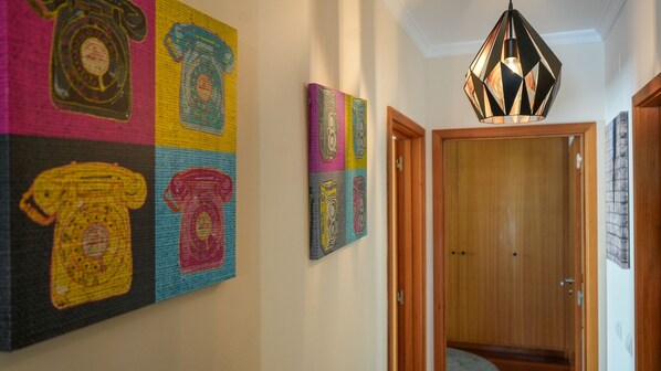 Un couloir avec une porte en bois, un luminaire suspendu et des œuvres d’art colorées accrochées au mur.