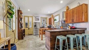 A kitchen with wooden cabinets, a central island, bar stools, and a large blue pot. - Charming Historic House w Heated Pool & Hot Tub 5 BR|3 BA (New Orleans)