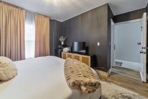 A bedroom with a large bed, a television on a wooden cabinet, and a door leading to another room.