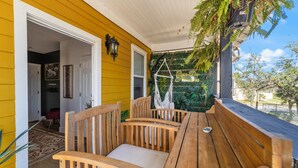 A wooden bench and table on a porch with yellow siding, a hanging chair, and a view of the street. - Casa de Teo (St. Augustine)