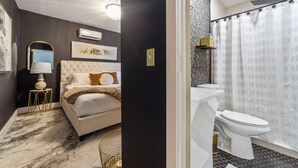 A bedroom with a bed, bedside table, lamp, and wall art. - Casa de Teo (St. Augustine)