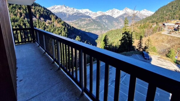 A balcony with a view of snow-capped mountains and a forested valley.
