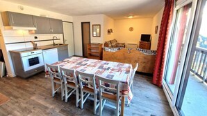 A compact kitchen with modern appliances, a dining table with chairs, and a cozy seating area with a sofa and curtains.