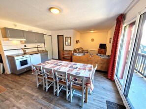 Una cocina compacta con electrodomésticos modernos, una mesa de comedor con sillas y una zona de estar acogedora con un sofá y cortinas.