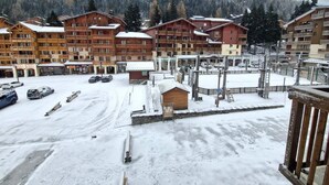 A snow-covered parking area with several wooden buildings, including a ski lift and a small wooden structure.