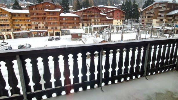 A view of a hotel with multiple wooden buildings, balconies, and a snowy landscape in the background.
