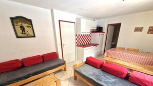 A compact room with two wooden beds with red and black bedding, a small kitchenette, and a checkered backsplash.