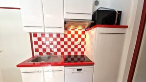 A compact kitchen with a red and white checkered backsplash, a built-in microwave, and a dishwasher.