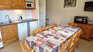 A compact kitchen with wooden cabinets, a microwave, a coffee maker, and a dining table with a checkered tablecloth. - 100m from ski slopes, 1st floor, balcony, ski locker, 48m², Valfréjus (Valfréjus)
