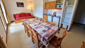A compact living space with a dining table, wooden chairs, a red sofa, a kitchen area with cabinets and a microwave, and a small bookshelf. - 100m from ski slopes, 1st floor, balcony, ski locker, 48m², Valfréjus (Valfréjus)
