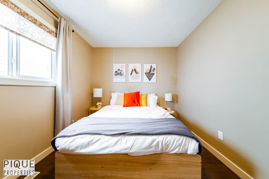 Ein Schlafzimmer mit einem Bett, zwei Nachttischen, einem Fenster mit Vorhängen und drei Wandbildern.