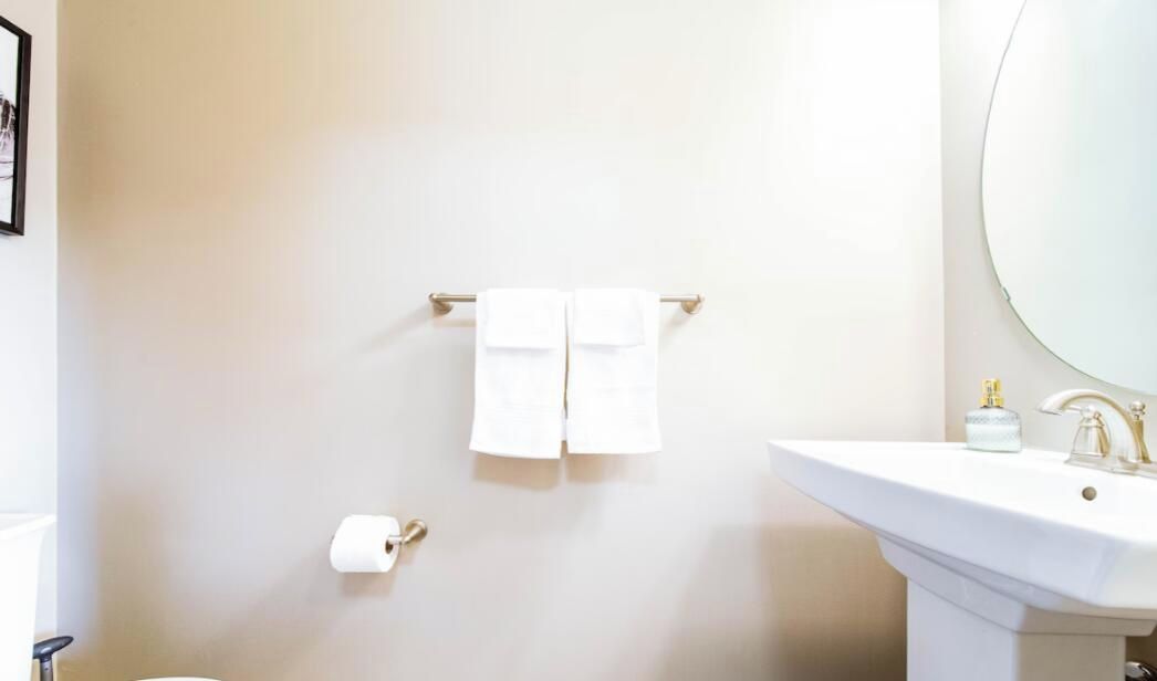 A bathroom with a white sink, a round mirror, and two white towels hanging on a towel bar.