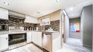 A modern kitchen with stainless steel appliances, a dishwasher, and a tiled backsplash. - Chic 6BDRM Getaway - KingBed - Patio - BBQ - Garage - Wifi (Edmonton)