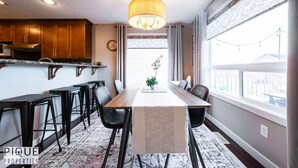A modern kitchen with wooden cabinets, a dining table with chairs, and a chandelier. - Chic 6BDRM Getaway - KingBed - Patio - BBQ - Garage - Wifi (Edmonton)