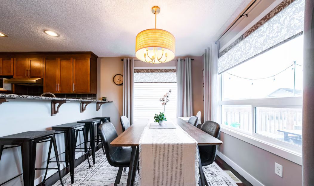 A modern kitchen with wooden cabinets, a dining table with chairs, and a chandelier.