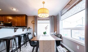 A modern kitchen with wooden cabinets, a dining table with chairs, and a chandelier.