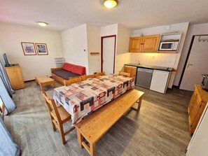 A compact living space with a dining table, benches, a sofa, a kitchenette, and a door. - Resort center, 1st floor, view open, balcony, tv, ski locker, 42m², Valfréjus (Valfréjus)