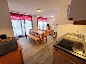 A compact kitchen with a dining table, wooden cabinets, a built-in stove, and a window with curtains. - Resort center, 1st floor, view open, balcony, tv, ski locker, 42m², Valfréjus (Valfréjus)