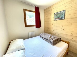 A single bed with white bedding, a red curtain, a framed picture on the wall, and a wooden panel wall.