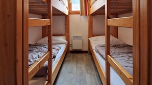 Quarto pequeno com beliches, uma janela com cortinas e uma luminária no teto.