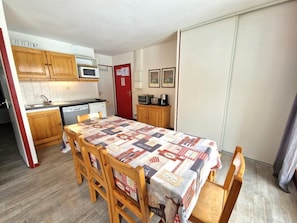 A compact kitchen with wooden cabinets, a microwave, and a small refrigerator. A dining table with a checkered tablecloth is set for four. - Resort center, 1st floor, view open, balcony, tv, ski locker, 42m², Valfréjus (Valfréjus)