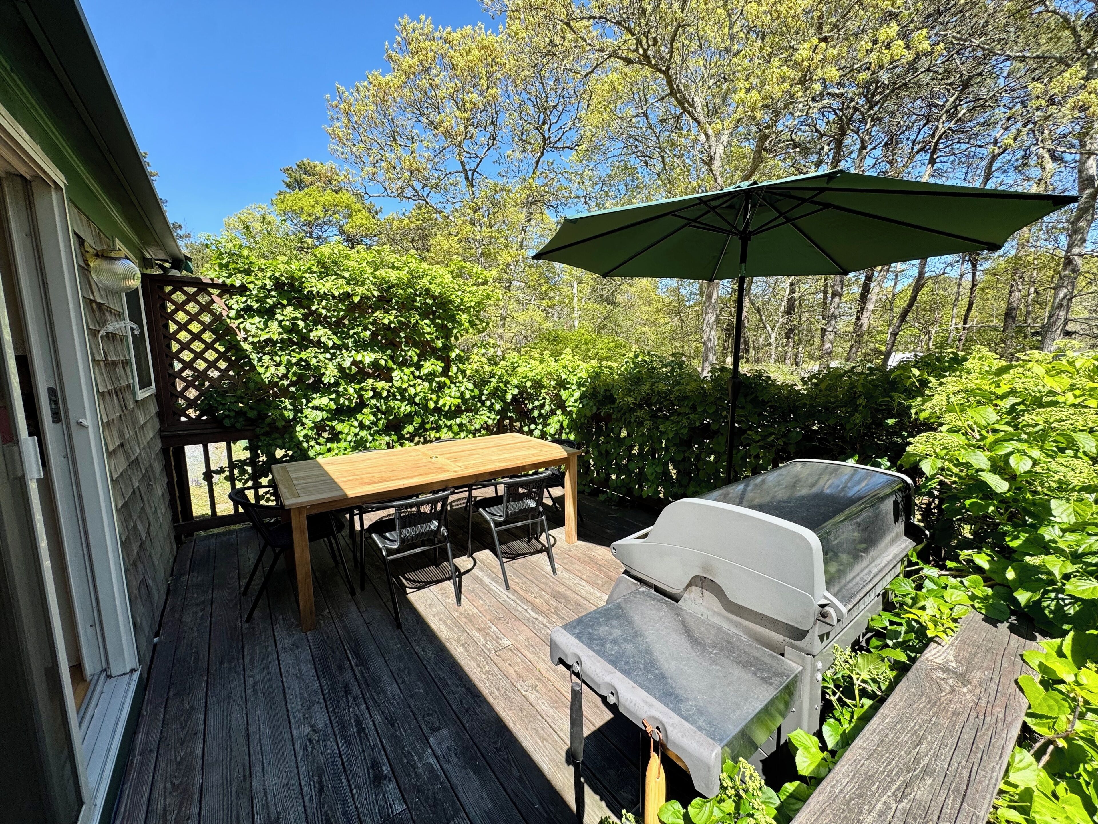 A wooden deck with a table and chairs, a barbecue grill, and an umbrella.