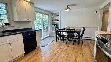 Una cocina moderna con armarios blancos, un lavavajillas negro, una mesa de comedor de madera con cuatro sillas y un horno empotrado.