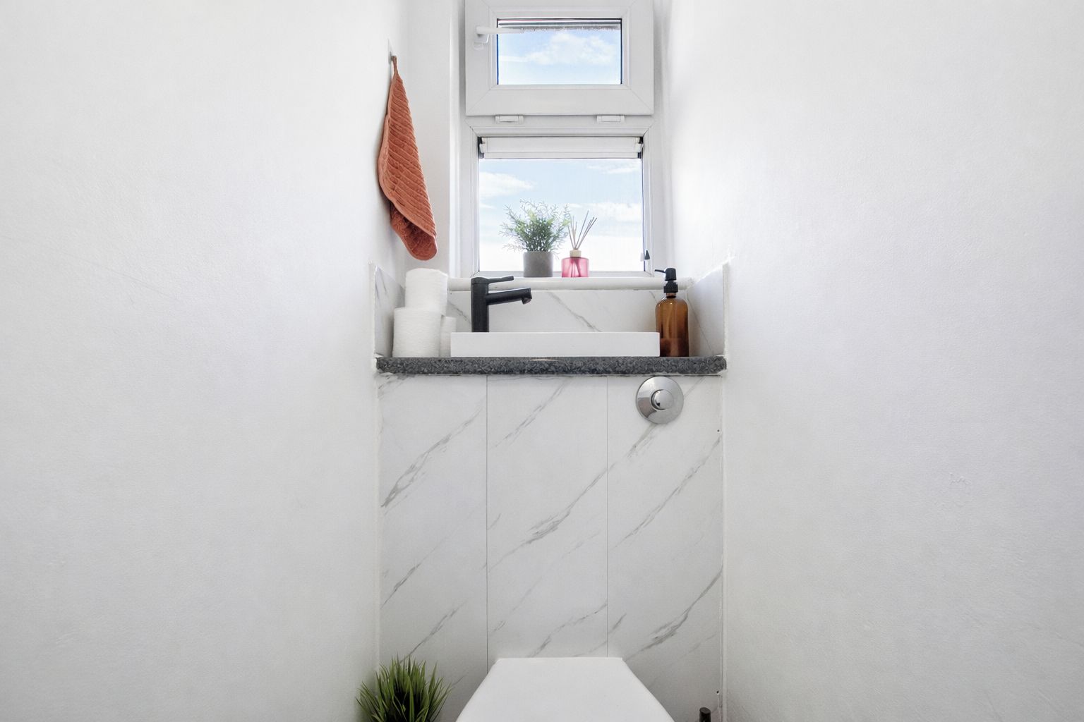 A bathroom with a white marble wall, a window, a towel rack, and a sink with a faucet.