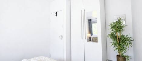 Une chambre à coucher avec un lit, une armoire blanche et une plante en pot.