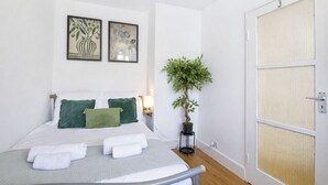 A hotel room with a bed, green pillows, a potted plant, and two framed artworks on the wall.