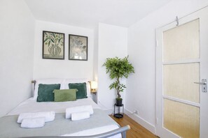 A hotel room with a bed, green pillows, a potted plant, and two framed artworks on the wall.