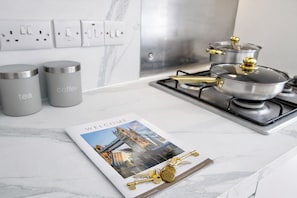 A kitchen with a gas stove, two stainless steel containers labeled 'tea' and 'coffee,' a welcome mat with a cityscape image, and a set of keys on a gold keychain.