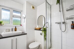 Un baño con lavamanos blanco, espejo, inodoro y ducha.