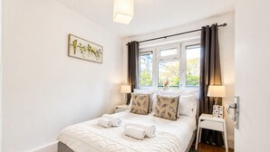 A neatly arranged bedroom with a bed, bedside lamps, a window with curtains, and a wall-mounted picture. - Central Square Apartments (London)