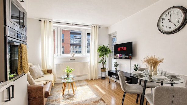 A modern living room with a sofa, coffee table, dining table, chairs, a TV, and a clock.