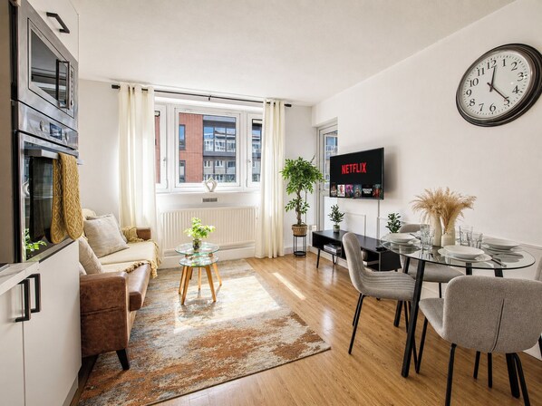 A modern living room with a sofa, coffee table, dining table, chairs, a TV, and a clock.