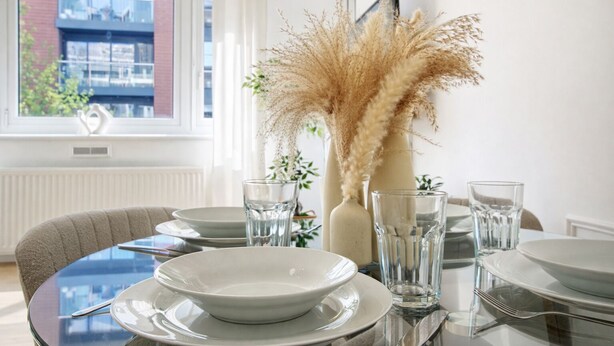A dining table set with plates, glasses, and a vase with pampas grass. - Central Square Apartments (London)