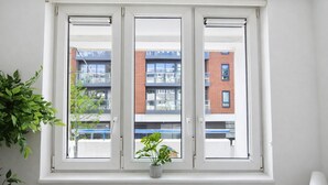 A window with three sections, a potted plant, and a view of a building with balconies. - Central Square Apartments (London)