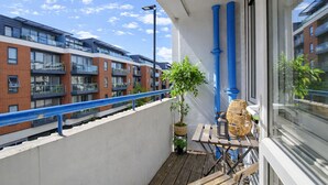 A balcony with a potted plant, a wicker chair, and a table. - Central Square Apartments (London)