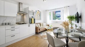 A modern kitchen with white cabinetry, a stove, and a microwave. There is a dining area with a glass table and chairs.