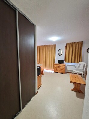 Ein gemütlicher, kleiner Wohnraum mit Schiebetür, einem weißen Sofa, einem Holztisch, einer TV-Konsole und einem Spiegel an der Wand.