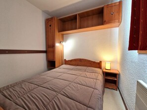 A bedroom with a bed, wooden headboard, built-in shelving, and a bedside lamp. - 100m from ski slopes, 2nd floor, balcony, ski locker, 36m², Valfréjus (Valfréjus)