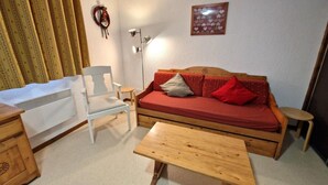 Un salon chaleureux avec un canapé en bois, un fauteuil blanc, une petite table et un radiateur.