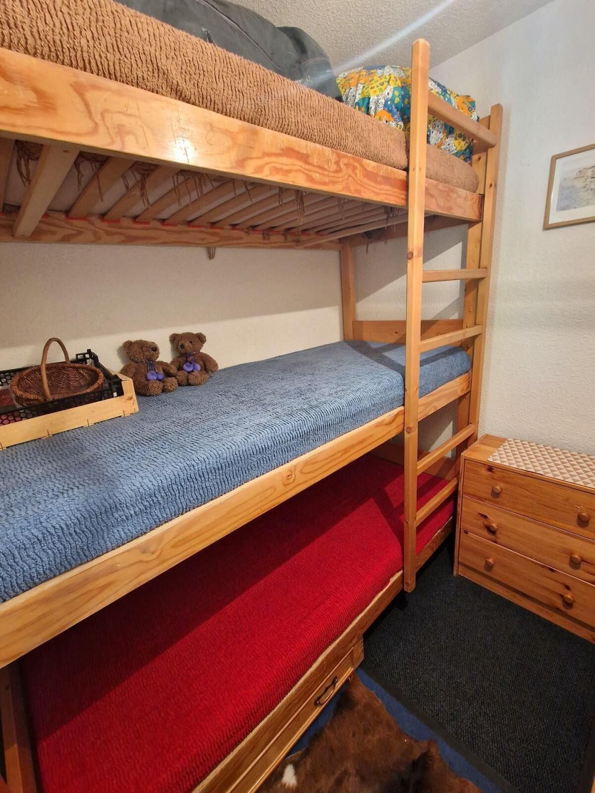 Ein Stockbett mit Holzlade, einer kleinen Holzkiste und zwei Teddybären auf dem untersten Bett.