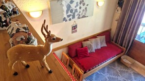 A cozy room with a red sofa, a small table with a deer figurine, and a wall-mounted light fixture.