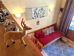Um quarto aconchegante com um sofá vermelho, uma mesa pequena com uma estatueta de veado e um aplique na parede.