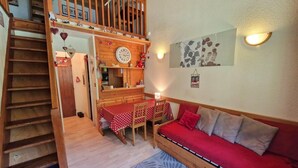 A cozy living area with a staircase, a dining table with chairs, a sofa, and a wall clock.
